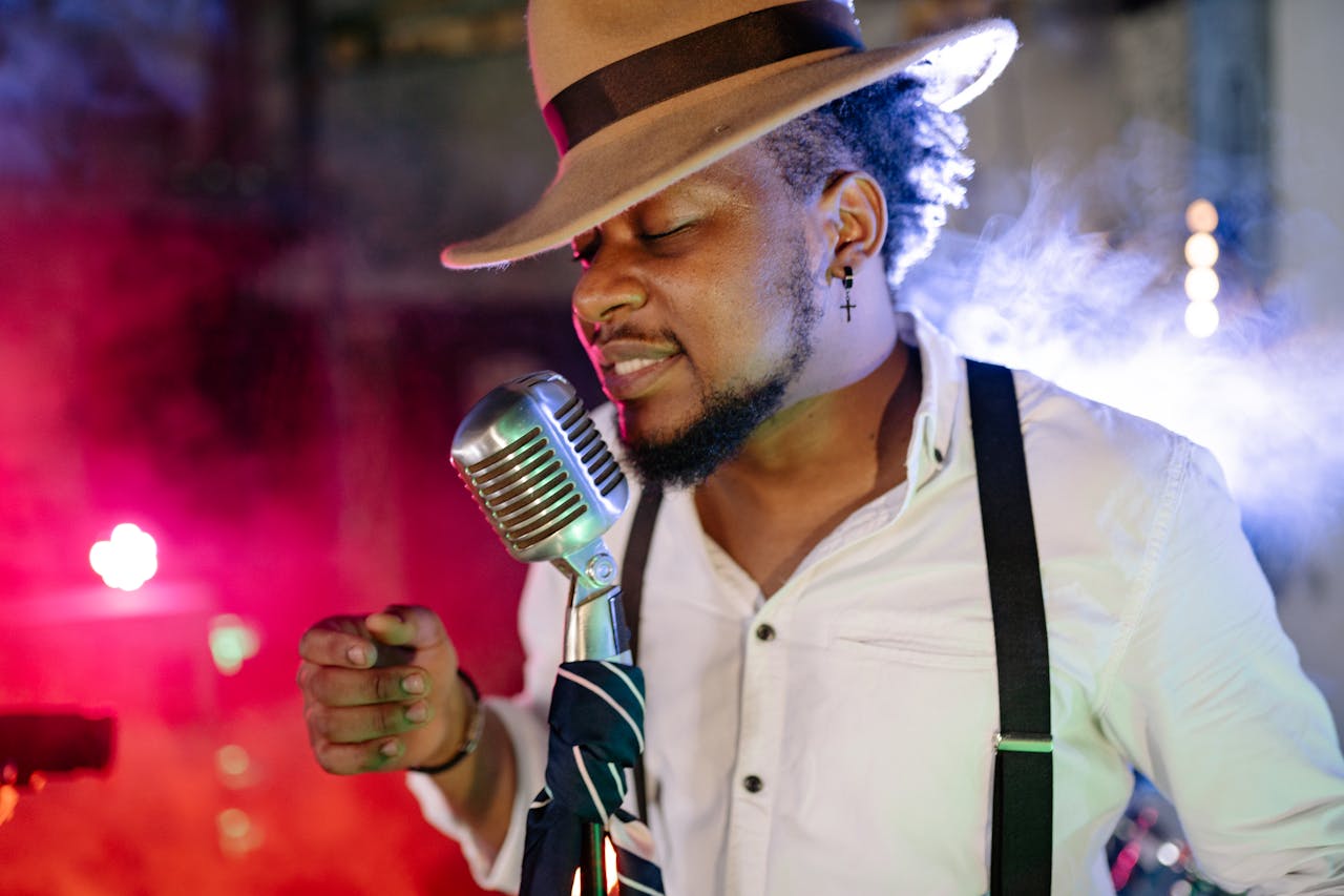 Black male singer with hat singing passionately into a vintage microphone on a vibrant stage.
